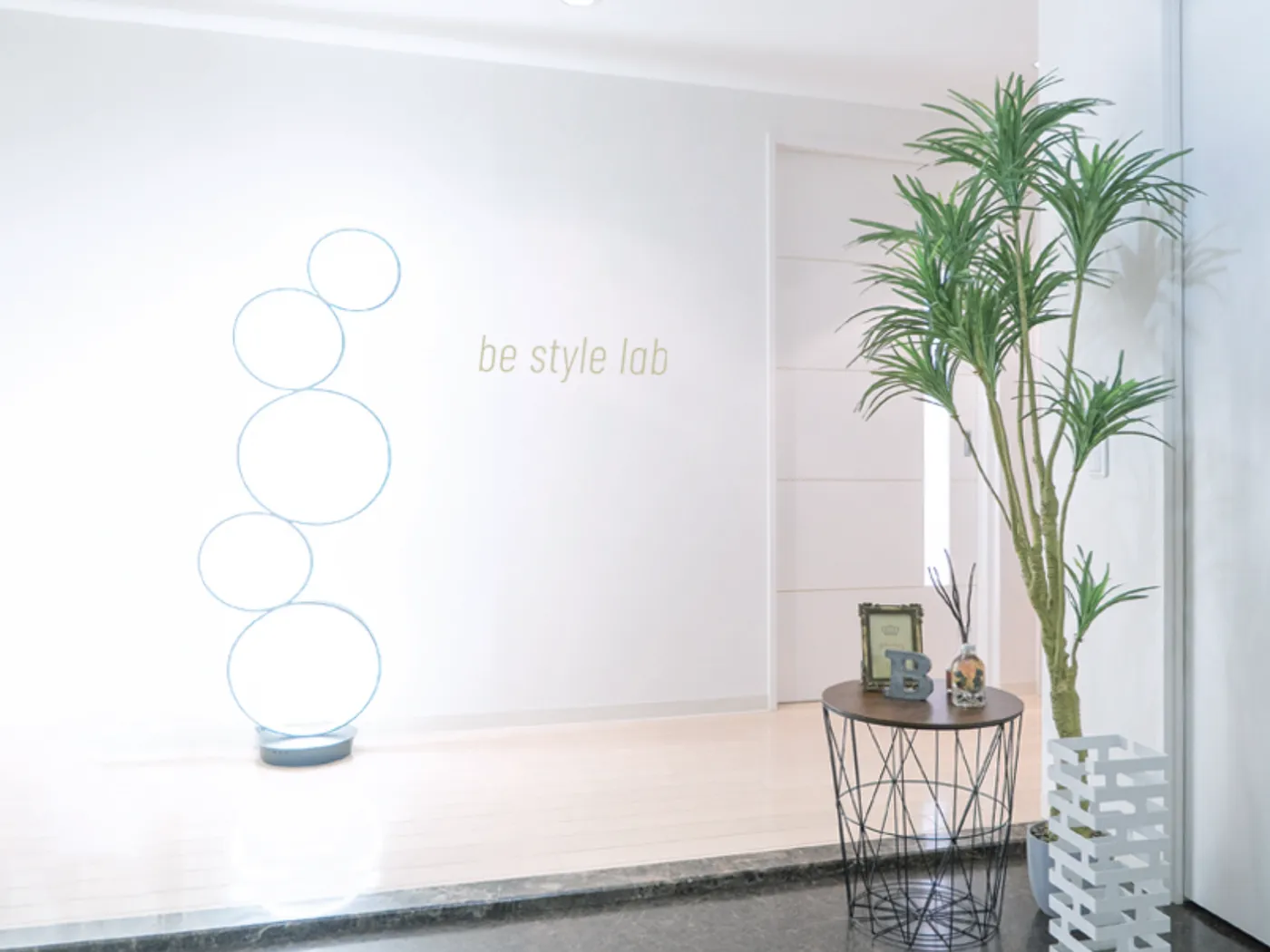 be style lab 名古屋のエントランス。白い壁のロゴと照明