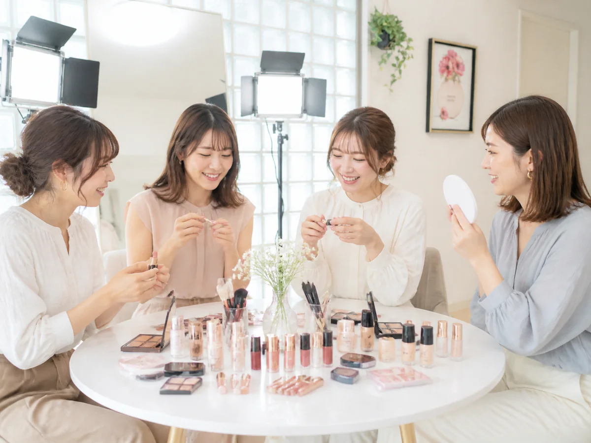 テーブルいっぱいのコスメを試しながら笑顔で話す4人の女性